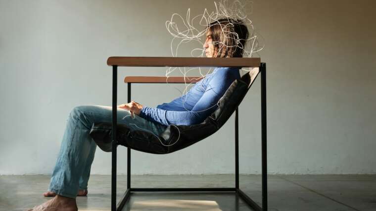 A seated person in a modern chair, with abstract wire-like shapes above their head.