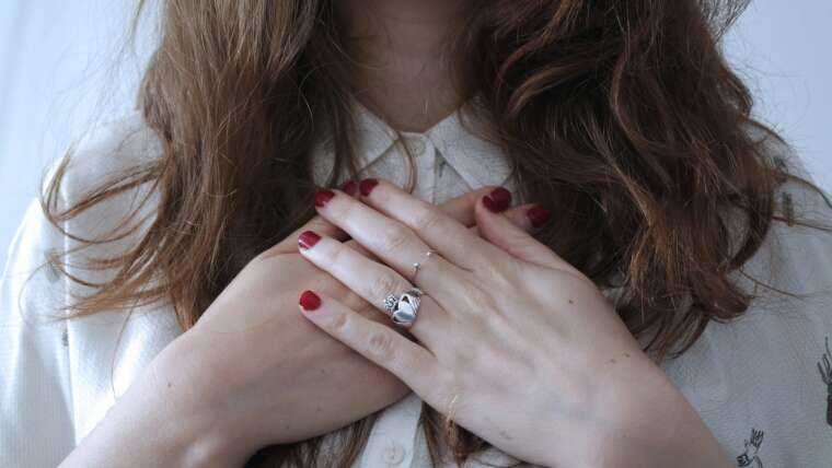 Hands with red nail polish clasped together on a chest, hair cascading over shoulders.