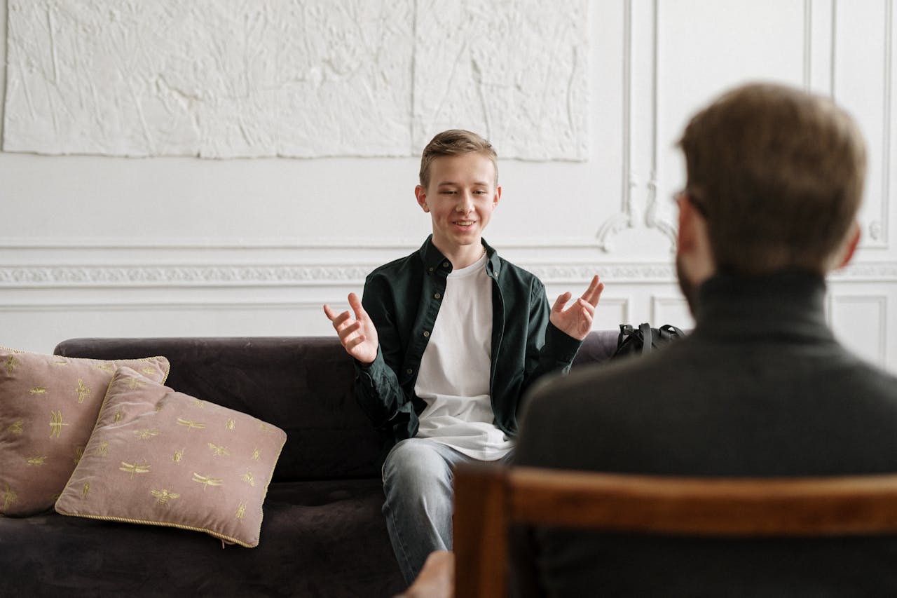 A young man in a green shirt smiles while gesturing during a conversation on a sofa.