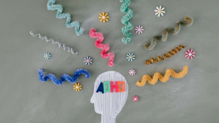 Colorful pipe cleaners and flowers surround a head outline with "ADHD" letters inside.